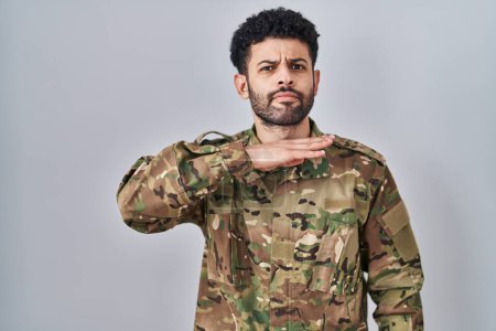 Photo for Arab man wearing camouflage army uniform cutting throat with hand as knife, threaten aggression with furious violence - Royalty Free Image