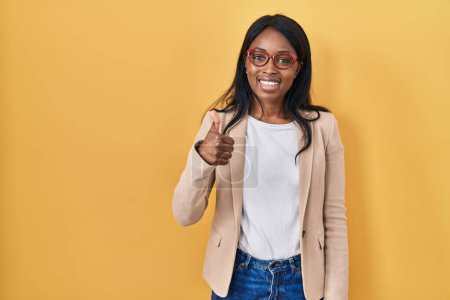 Photo for African young woman wearing glasses doing happy thumbs up gesture with hand. approving expression looking at the camera showing success. - Royalty Free Image