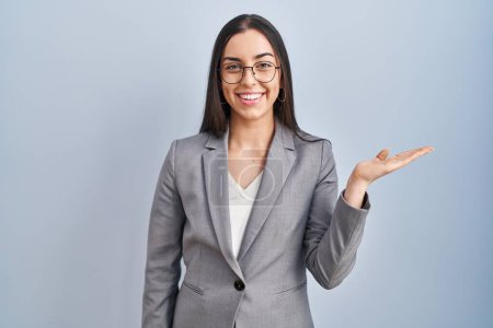 Foto de Mujer de negocios hispana con gafas sonriendo alegre presentando y señalando con la palma de la mano mirando a la cámara. - Imagen libre de derechos