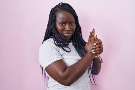 Photo for Young african woman standing over pink background holding symbolic gun with hand gesture, playing killing shooting weapons, angry face - Royalty Free Image