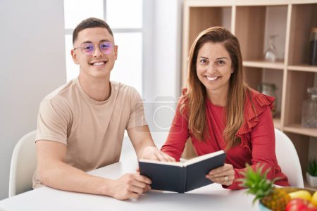 Foto de Man and woman mother and son reading book sitting on table at home - Imagen libre de derechos