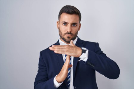 Téléchargez les photos : Bel homme hispanique portant costume et cravate faire le temps geste avec les mains, visage frustré et sérieux - en image libre de droit