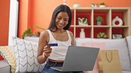 Foto de Mujer afroamericana de compras con portátil y tarjeta de crédito sentado en el sofá en casa - Imagen libre de derechos