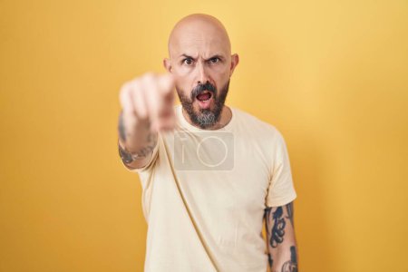Téléchargez les photos : Homme hispanique avec des tatouages debout sur fond jaune pointant mécontent et frustré à la caméra, en colère et furieux contre vous - en image libre de droit
