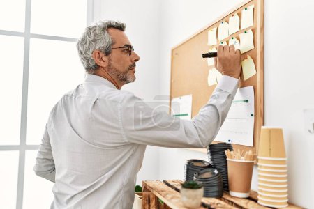 Foto de Hombre de pelo gris de mediana edad trabajador de negocios que escribe en el tablero de corcho en la oficina - Imagen libre de derechos