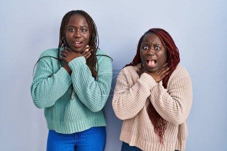 Téléchargez les photos : Deux femmes africaines debout sur fond bleu criant suffoquer parce que l'étranglement douloureux. problème de santé. concept d'asphyxie et de suicide. - en image libre de droit