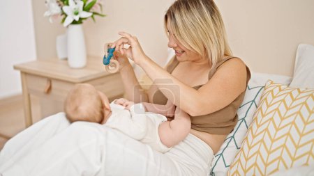 Photo for Mother and daughter sitting on bed together playing with ratlle at bedroom - Royalty Free Image