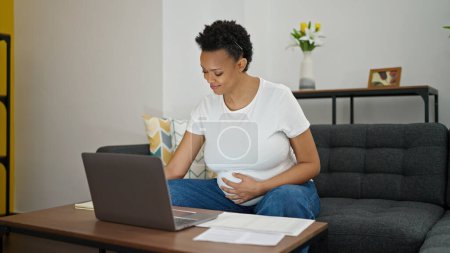 Foto de Mujer embarazada joven sentada en el sofá haciendo trabajo en línea en casa - Imagen libre de derechos