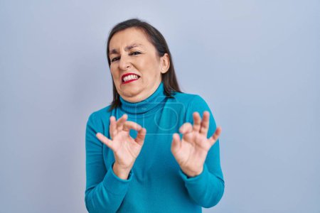 Foto de Mujer hispana de mediana edad de pie sobre un fondo aislado expresión disgustada, disgustada y temerosa haciendo cara de asco debido a la reacción de aversión. con las manos levantadas - Imagen libre de derechos