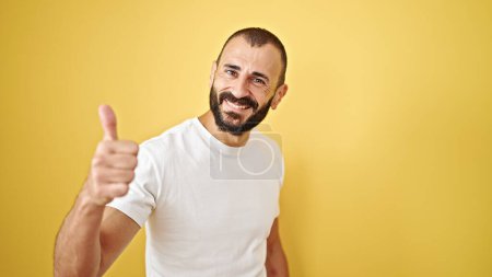 Foto de Joven hombre hispano sonriendo con el pulgar hacia arriba sobre el aislado fondo amarillo - Imagen libre de derechos