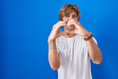 Photo for Middle age man standing over blue background smiling in love doing heart symbol shape with hands. romantic concept. - Royalty Free Image