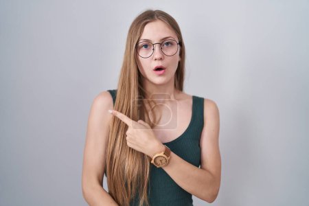 Photo for Young caucasian woman standing over white background surprised pointing with finger to the side, open mouth amazed expression. - Royalty Free Image