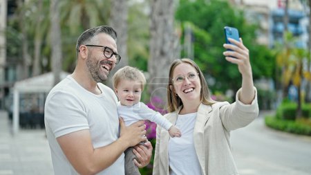 Téléchargez les photos : Famille de mère, père et bébé souriant prendre selfie avec le téléphone à la rue - en image libre de droit