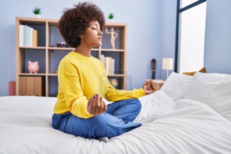 Foto de Mujer afroamericana haciendo ejercicio de yoga sentada en la cama en el dormitorio - Imagen libre de derechos