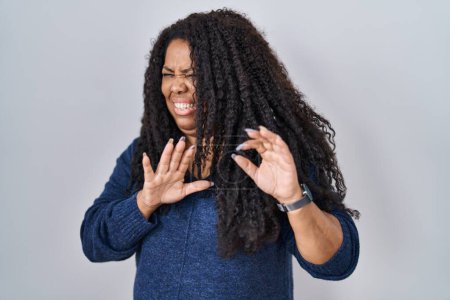 Photo for Plus size hispanic woman standing over white background disgusted expression, displeased and fearful doing disgust face because aversion reaction. with hands raised - Royalty Free Image