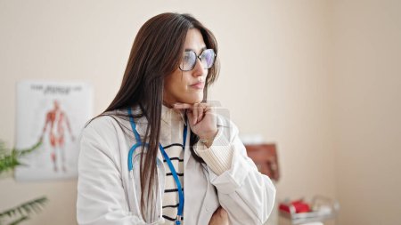 Téléchargez les photos : Jeune belle femme hispanique médecin debout avec doute expression pensée à la clinique - en image libre de droit