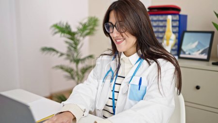 Foto de Joven hermosa mujer hispana médico utilizando portátil de trabajo en la clínica - Imagen libre de derechos