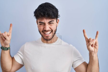 Photo for Hispanic man with beard standing over white background shouting with crazy expression doing rock symbol with hands up. music star. heavy music concept. - Royalty Free Image