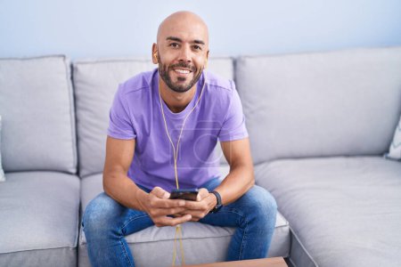 Photo for Young bald man listening to music sitting on sofa at home - Royalty Free Image