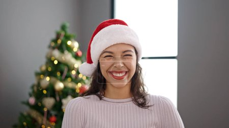Photo for Young beautiful hispanic woman smiling  by christmas tree at home - Royalty Free Image