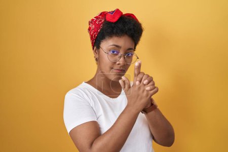 Photo for Young african american woman standing over yellow background holding symbolic gun with hand gesture, playing killing shooting weapons, angry face - Royalty Free Image