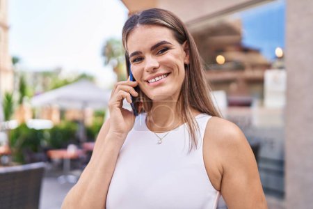 Foto de Joven hermosa mujer hispana sonriendo confiada hablando en el teléfono inteligente en la terraza de la cafetería - Imagen libre de derechos
