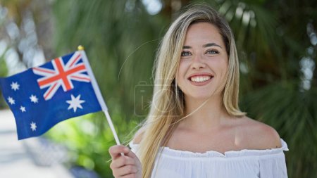 Photo for Young blonde woman smiling confident holding australia flag at park - Royalty Free Image