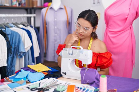 Photo for Hispanic young woman dressmaker designer using sewing machine pointing to the eye watching you gesture, suspicious expression - Royalty Free Image
