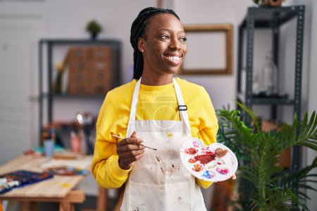 Foto de Mujer afroamericana artista sonriendo confiado sosteniendo pincel y paleta en el estudio de arte - Imagen libre de derechos