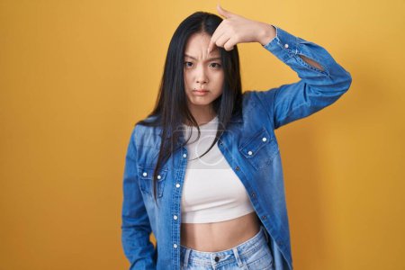 Téléchargez les photos : Jeune femme asiatique debout sur fond jaune pointant malheureux de boutons sur le front, infection laide de la tête noire. acné et problème de peau - en image libre de droit