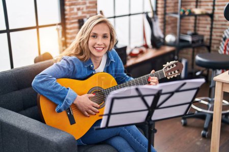 Foto de Joven mujer rubia músico tocando guitarra clásica en el estudio de música - Imagen libre de derechos