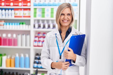 Photo for Young blonde woman pharmacist smiling confident holding clipboard at pharmacy - Royalty Free Image