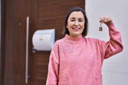 Foto de Mujer de mediana edad sonriendo confiada sosteniendo la llave de un nuevo hogar en la calle - Imagen libre de derechos