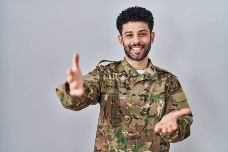 Téléchargez les photos : Arabe homme portant uniforme de camouflage armée souriant joyeuse offrant mains donnant assistance et acceptation. - en image libre de droit