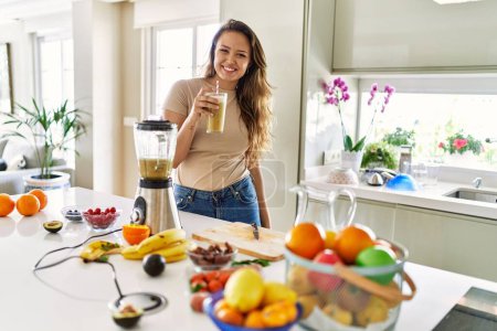 Photo for Young beautiful hispanic woman smiling confident holding glass of vegetable smoothie at the kitchen - Royalty Free Image