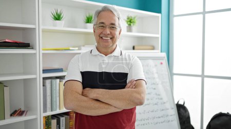 Téléchargez les photos : Homme d'âge moyen avec des cheveux gris enseignant debout par tableau blanc à l'université salle de classe - en image libre de droit