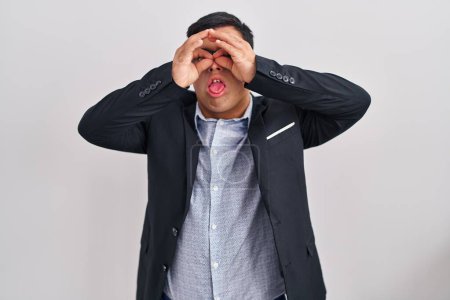 Photo for Young hispanic man with down syndrome wearing business style doing ok gesture like binoculars sticking tongue out, eyes looking through fingers. crazy expression. - Royalty Free Image