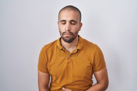 Téléchargez les photos : Homme hispanique avec la barbe debout sur fond blanc avec la main sur le ventre parce que l'indigestion, la maladie douloureuse se sent mal. concept de douleur. - en image libre de droit