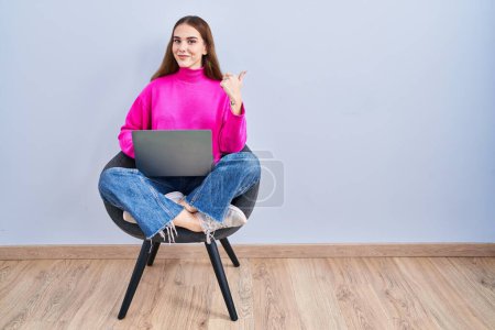 Téléchargez les photos : Jeune fille hispanique travaillant à l'aide d'un ordinateur portable pointant vers le dos derrière avec la main et les pouces vers le haut, souriant confiant - en image libre de droit