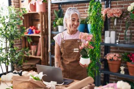 Photo for Middle age grey-haired woman florist using laptop holding plant at florist - Royalty Free Image