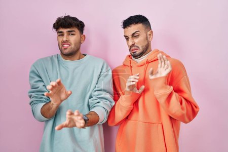 Photo for Young hispanic gay couple standing over pink background disgusted expression, displeased and fearful doing disgust face because aversion reaction. - Royalty Free Image