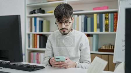 Téléchargez les photos : Jeune homme hispanique étudiant utilisant un smartphone dans une salle de classe universitaire - en image libre de droit