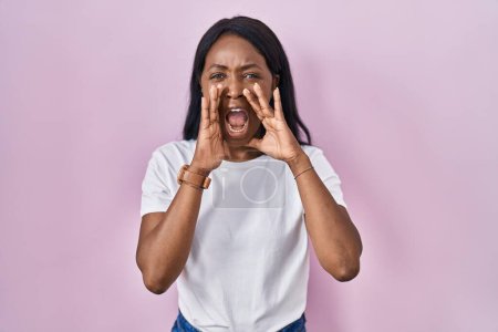 Téléchargez les photos : Africaine jeune femme portant casual t-shirt blanc criant en colère à haute voix avec les mains sur la bouche - en image libre de droit