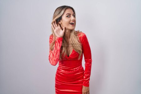 Photo for Young blonde woman wearing sexy party dress smiling with hand over ear listening an hearing to rumor or gossip. deafness concept. - Royalty Free Image