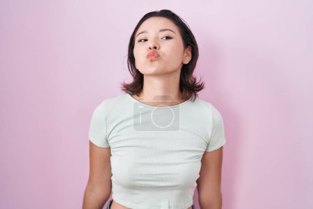 Téléchargez les photos : Jeune femme hispanique debout sur fond rose regardant la caméra souffler un baiser sur l'air étant belle et sexy. expression d'amour. - en image libre de droit
