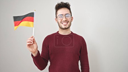 Téléchargez les photos : Jeune homme hispanique souriant confiant tenant drapeau deutschland sur fond blanc isolé - en image libre de droit