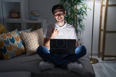 Photo for Young hispanic man using laptop at home at night beckoning come here gesture with hand inviting welcoming happy and smiling - Royalty Free Image