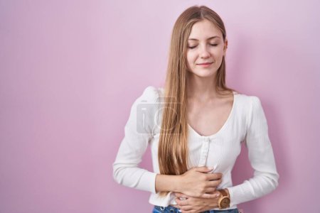 Photo for Young caucasian woman standing over pink background with hand on stomach because indigestion, painful illness feeling unwell. ache concept. - Royalty Free Image