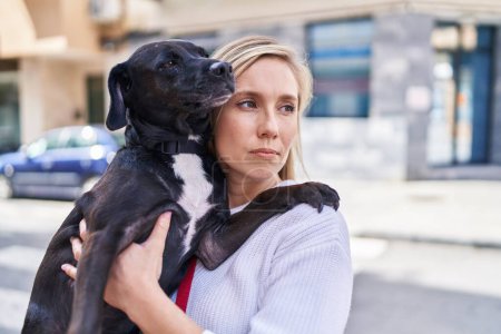 Téléchargez les photos : Jeune femme blonde étreignant chien debout à la rue - en image libre de droit