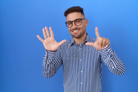 Téléchargez les photos : Homme hispanique avec barbe portant des lunettes montrant et pointant vers le haut avec les doigts numéro sept tout en souriant confiant et heureux. - en image libre de droit